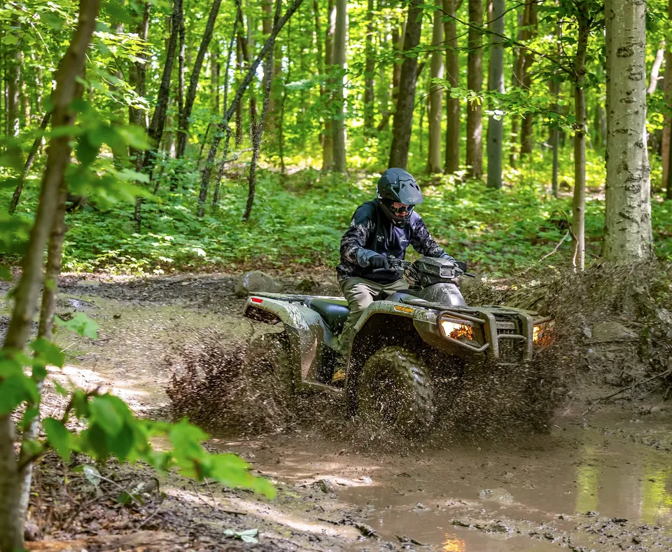 A rider on a Honda FourTrax Rubicon 700 splashing through a muddy trail in the woods